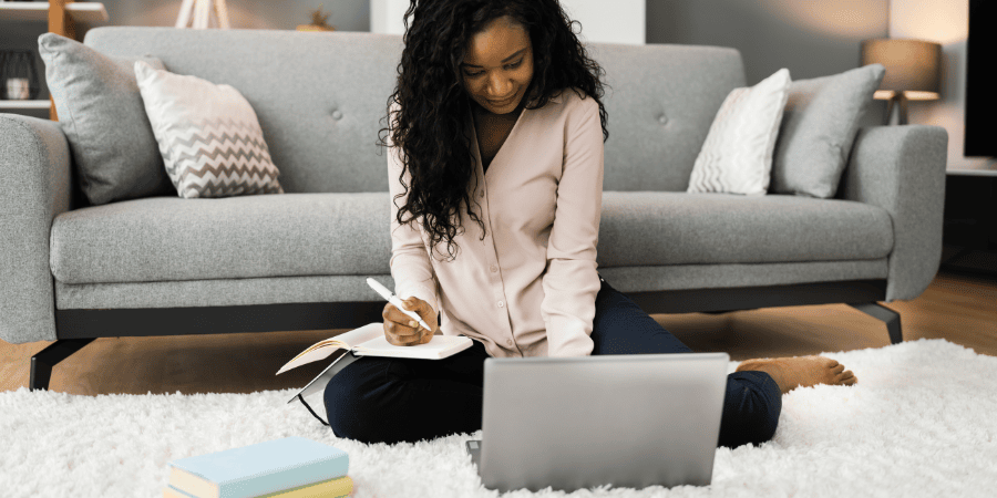 Image of a black woman sitting on the floor, with a laptop in front of her & notebook/journal on her lap as if on a coaching call