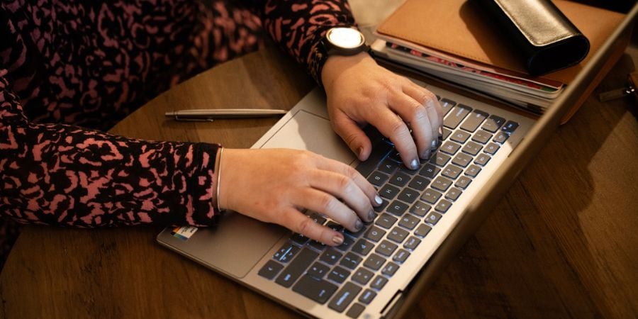 Image of a black woman sitting on the floor, with a laptop in front of her & notebook/journal on her lap as if on a coaching call. It gives the impression of someone working through their trauma and going on a journey of recovery, rediscovery and reconnection.